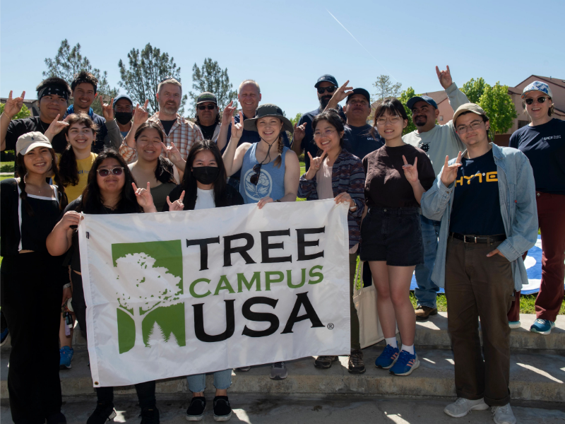 people gathered holding a banner that reads tree campus usa
