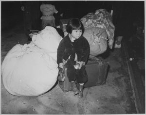 Japanese-American child with family belongings en route to California internment camp (Spring 1942). Image via U.S. National Archives and Records Administration.